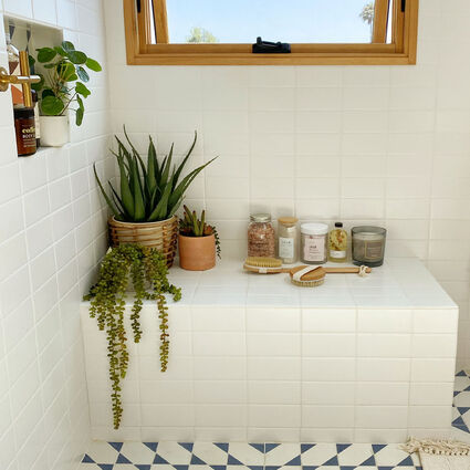 Spacious white tiled bathroom corner with potted plants
