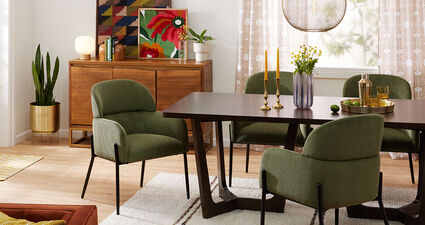 Image of a colorful dining room space featuring the Reynold Burnt Black Oak Wood Tri Leg Base Dining Table and green Alba Corduroy Upholstered Dining Armchairs.
