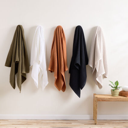 Four bath towels hanging on hooks in a variety of colors