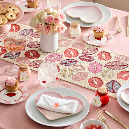 Table set for Valentine's Day or a "Galentine" party with lip-print beaded table runner, heart dishes, and a pink and red heart and lip theme